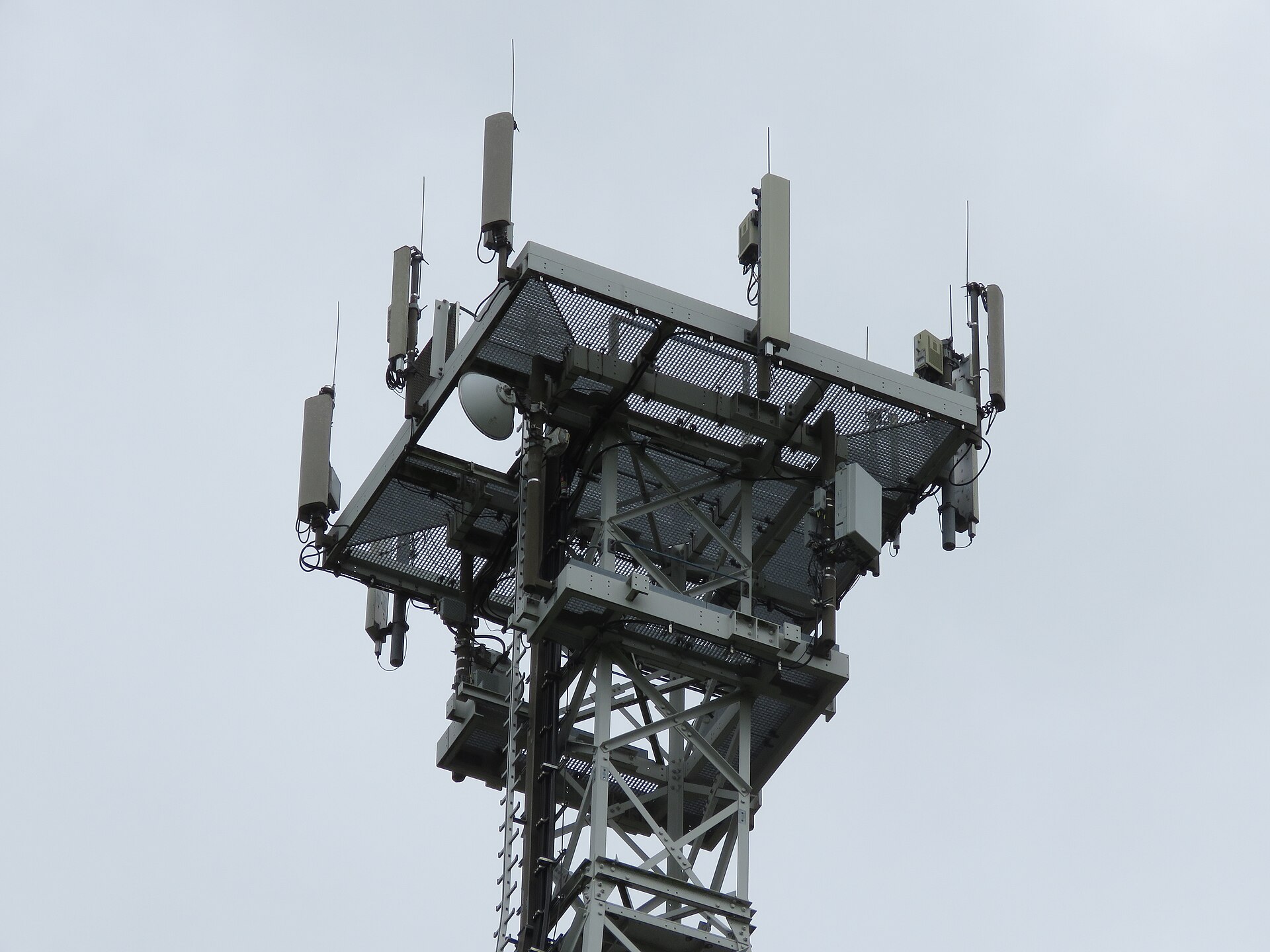 Foto de archivo: la parte superior de una torre de telecomunicaciones metálica con varias antenas y equipos de red montados, contra un cielo gris nublado.
